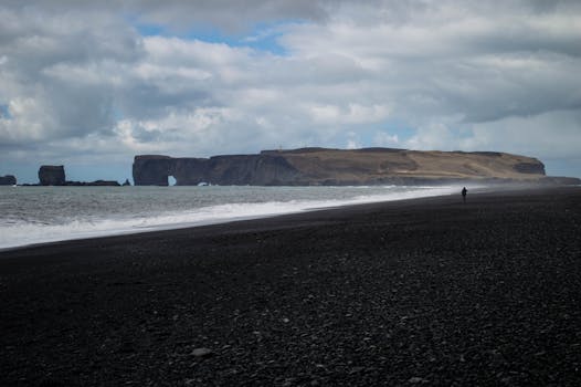 Scenic view of Dyrhólaey from a black sand beach in Iceland with cloudy skies.