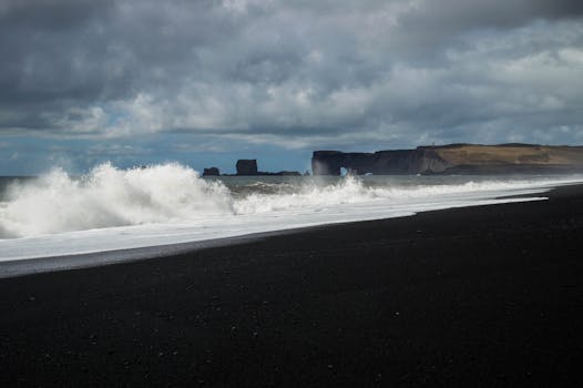 Dramatic waves crash on a black sand beach in Iceland under a cinematic sky.