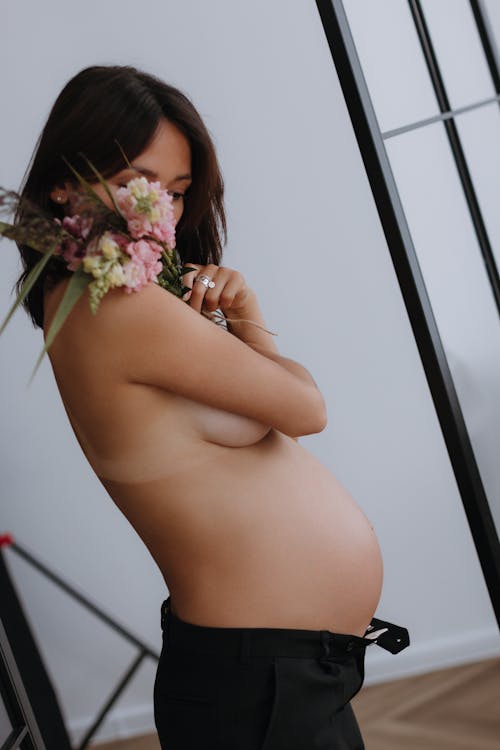 A Topless Pregnant Woman Covering her Face with Flowers