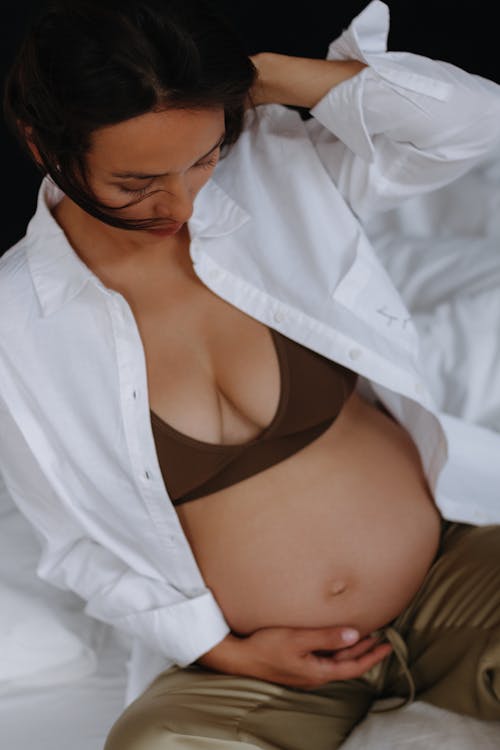 Pregnant Woman in White Unbuttoned Shirt Touching her Belly