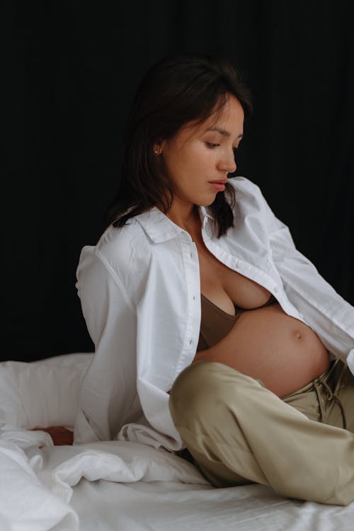 Pregnant Woman in White Unbuttoned Shirt Sitting on a Bed