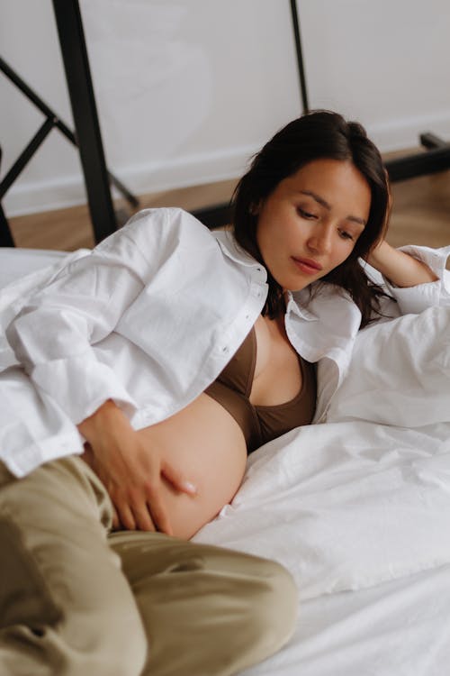 Pregnant Brunette Woman in White Shirt Lying in Bed