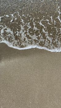Close-up of waves meeting sandy beach, showcasing textures of water and sand.