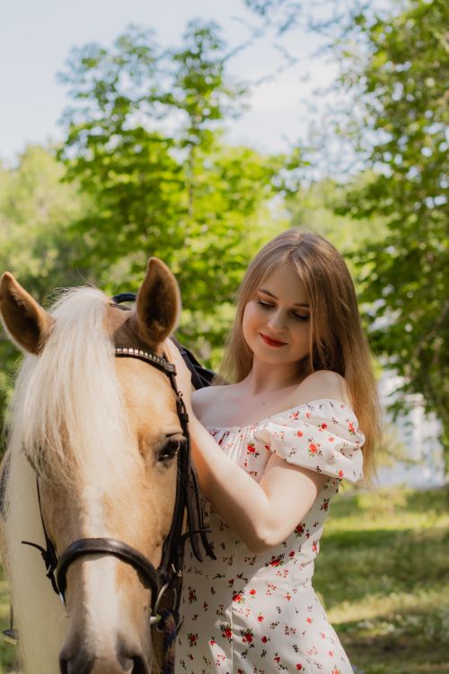 Free A young woman in a floral dress lovingly embraces a horse in a sunny outdoor setting. Stock Photo