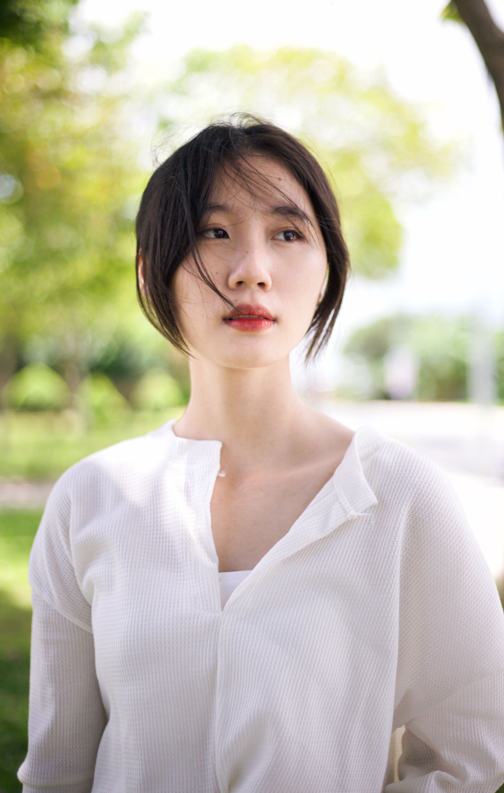 Casual outdoor portrait of a woman with brown hair in a white blouse.