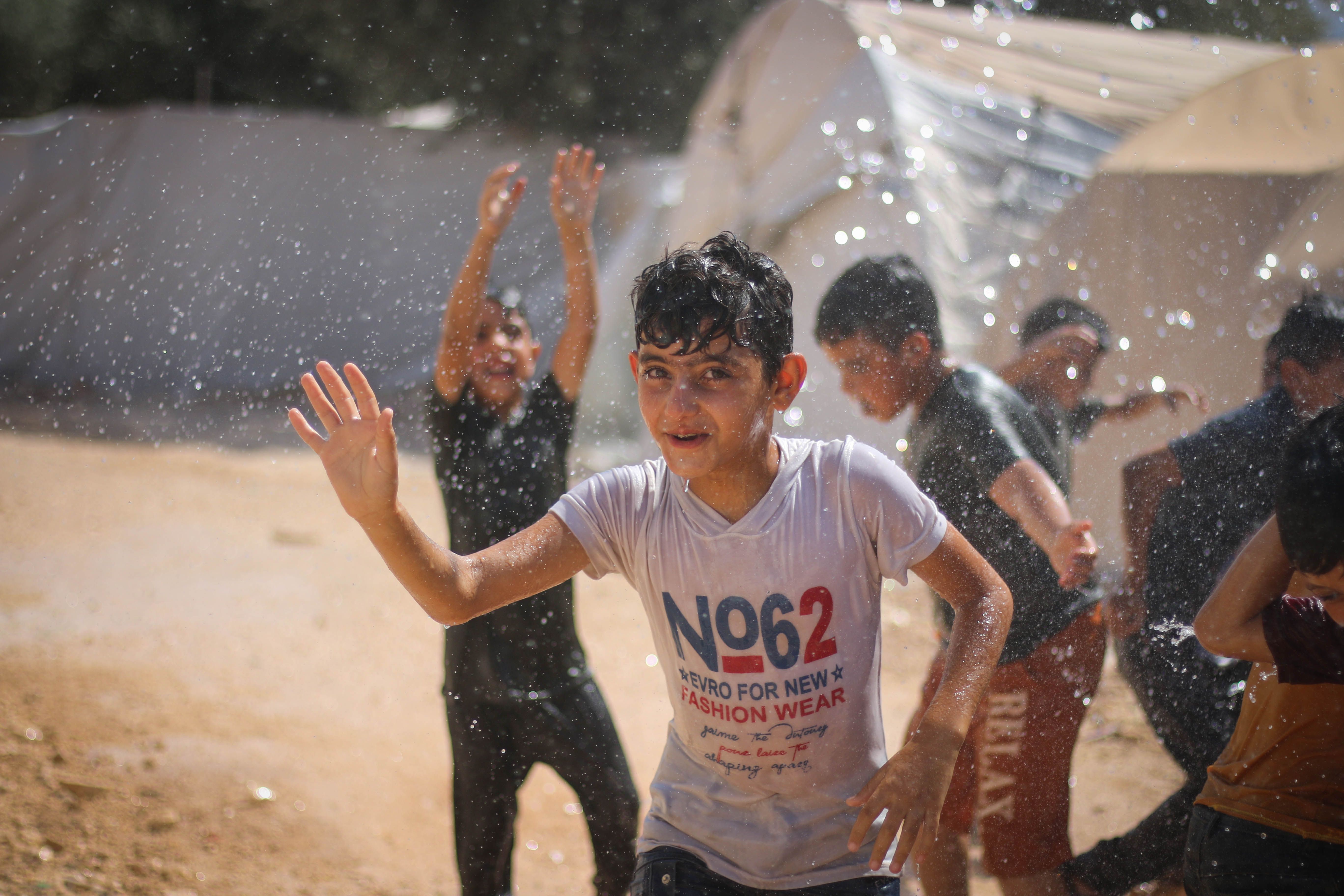 Children having fun splashing in water at a refugee camp in Idlib, Syria during summer.