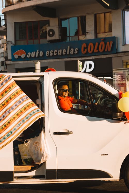 Free A man driving a decorated white van in a sunny urban location, evoking a festive mood. Stock Photo