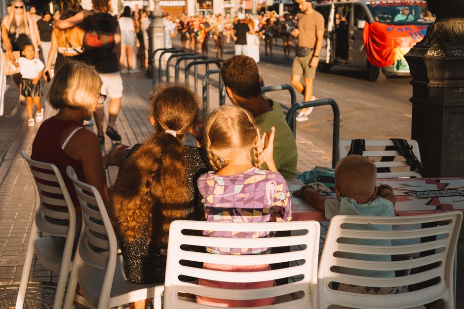 Vista desde atrás de una familia multigeneracional sentada junta en un entorno urbano animado.