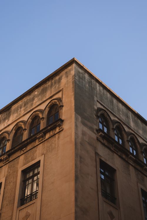 Free Low angle view of an antique building corner with arched windows under a clear sky. Stock Photo