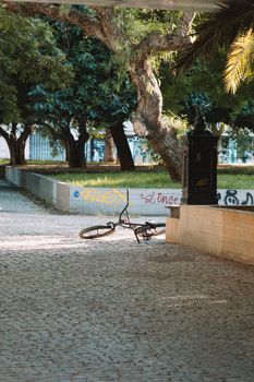 A serene urban park scene featuring an abandoned bicycle lying on a cobblestone path with green surroundings.