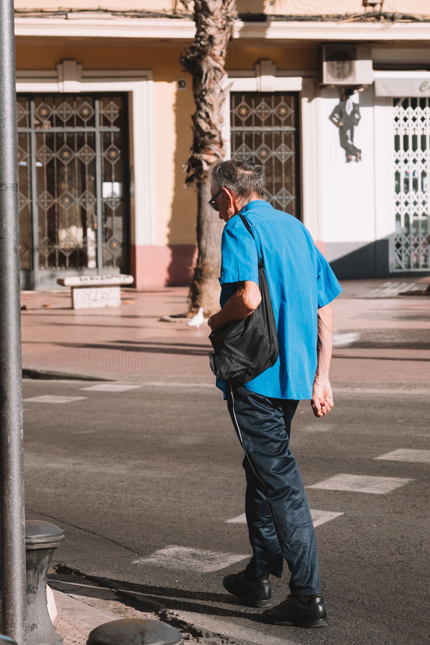 A senior man walking along a sunlit city street