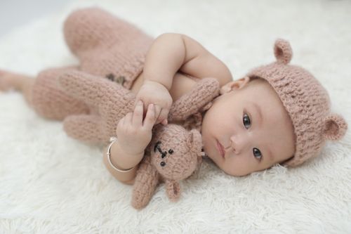 Free Cute baby wearing knit bear hat and holding teddy bear on soft background. Stock Photo