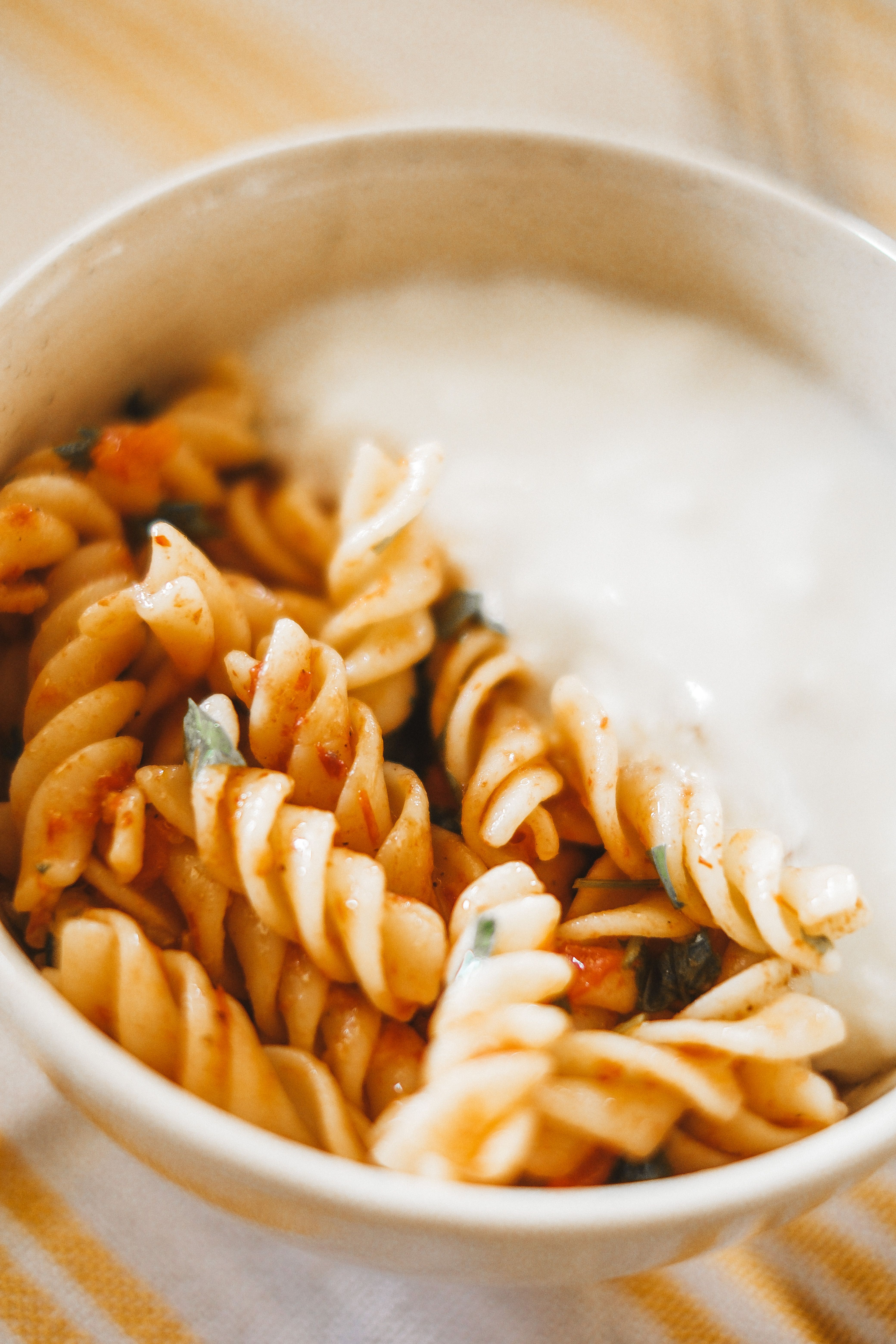 Close-up of a bowl of rotini pasta with tomato sauce and a side of creamy sauce.