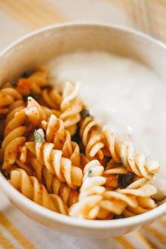 Close-up of a bowl of rotini pasta with tomato sauce and a side of creamy sauce.