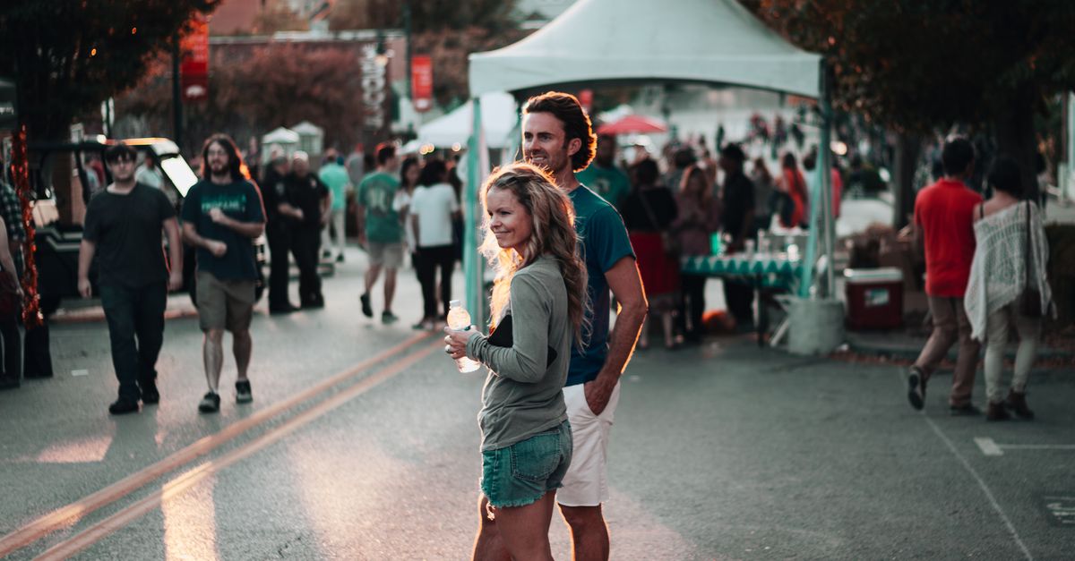 A couple enjoys a lively street festival in Fayetteville, Arkansas, surrounded by people and vibrant atmosphere.