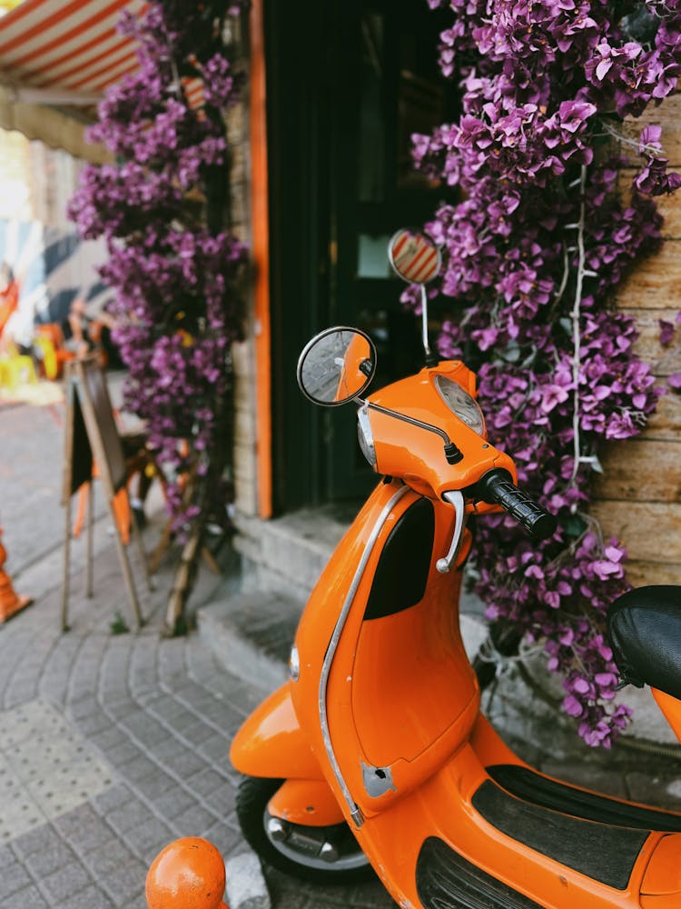 Orange Vespa And Purple Flowers On Wall Behind