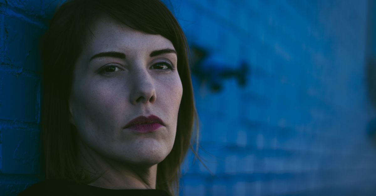 A woman with brown hair poses at night against a blue brick wall in Fayetteville, AR.