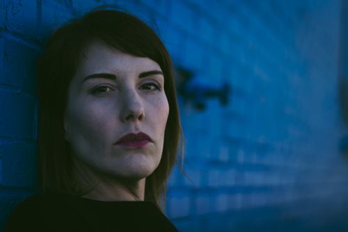 Free A woman with brown hair poses at night against a blue brick wall in Fayetteville, AR. Stock Photo