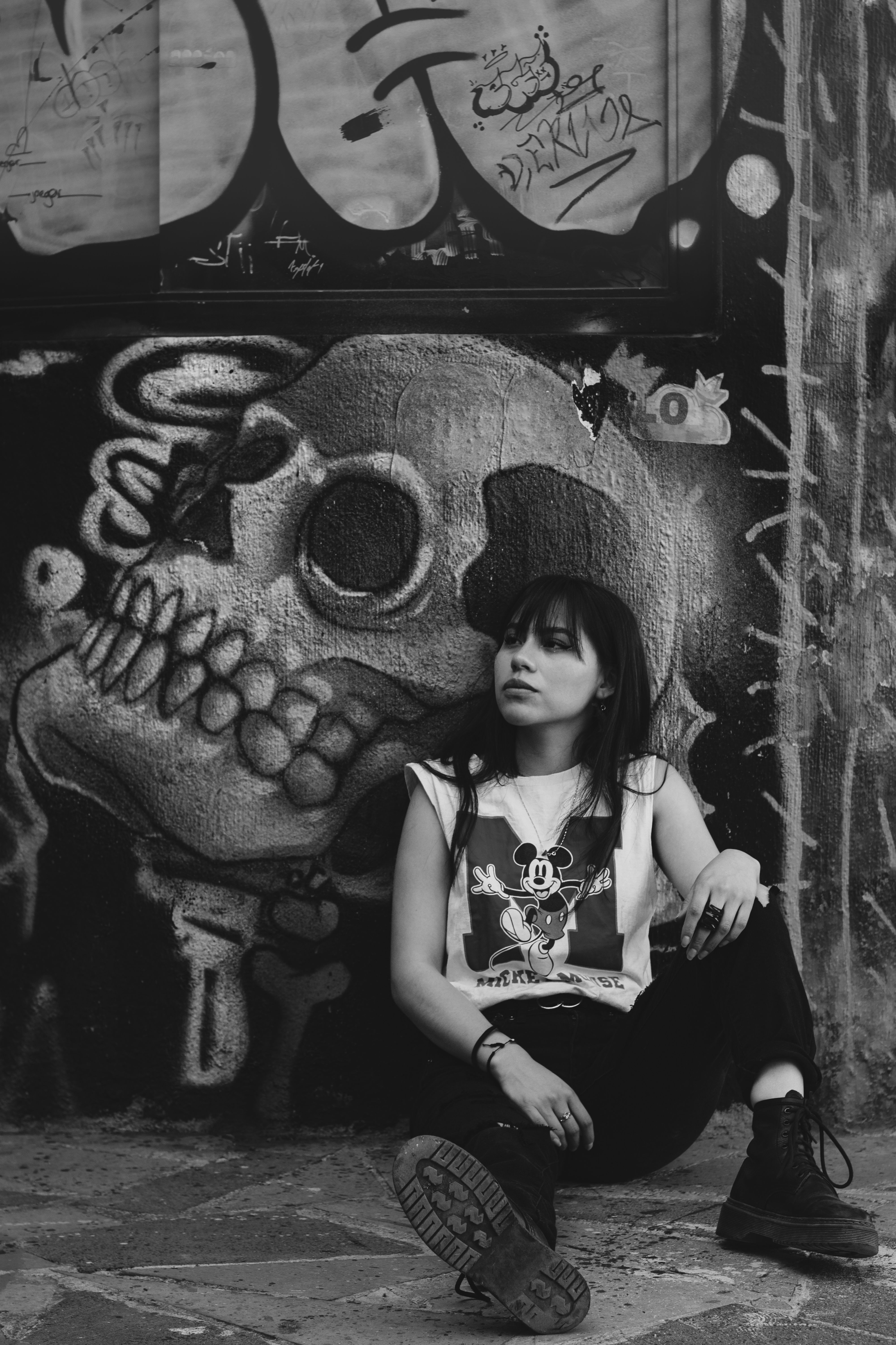 Woman sitting against graffiti wall featuring skull art in Mexico City, urban and edgy feel.