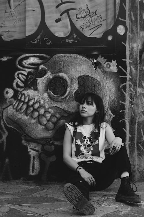 Woman Sitting by Skull Graffiti on Wall in Black and White