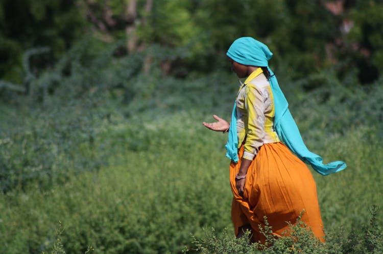 Woman In Turquoise Headscarf And Orange Skirt Standing In Grass