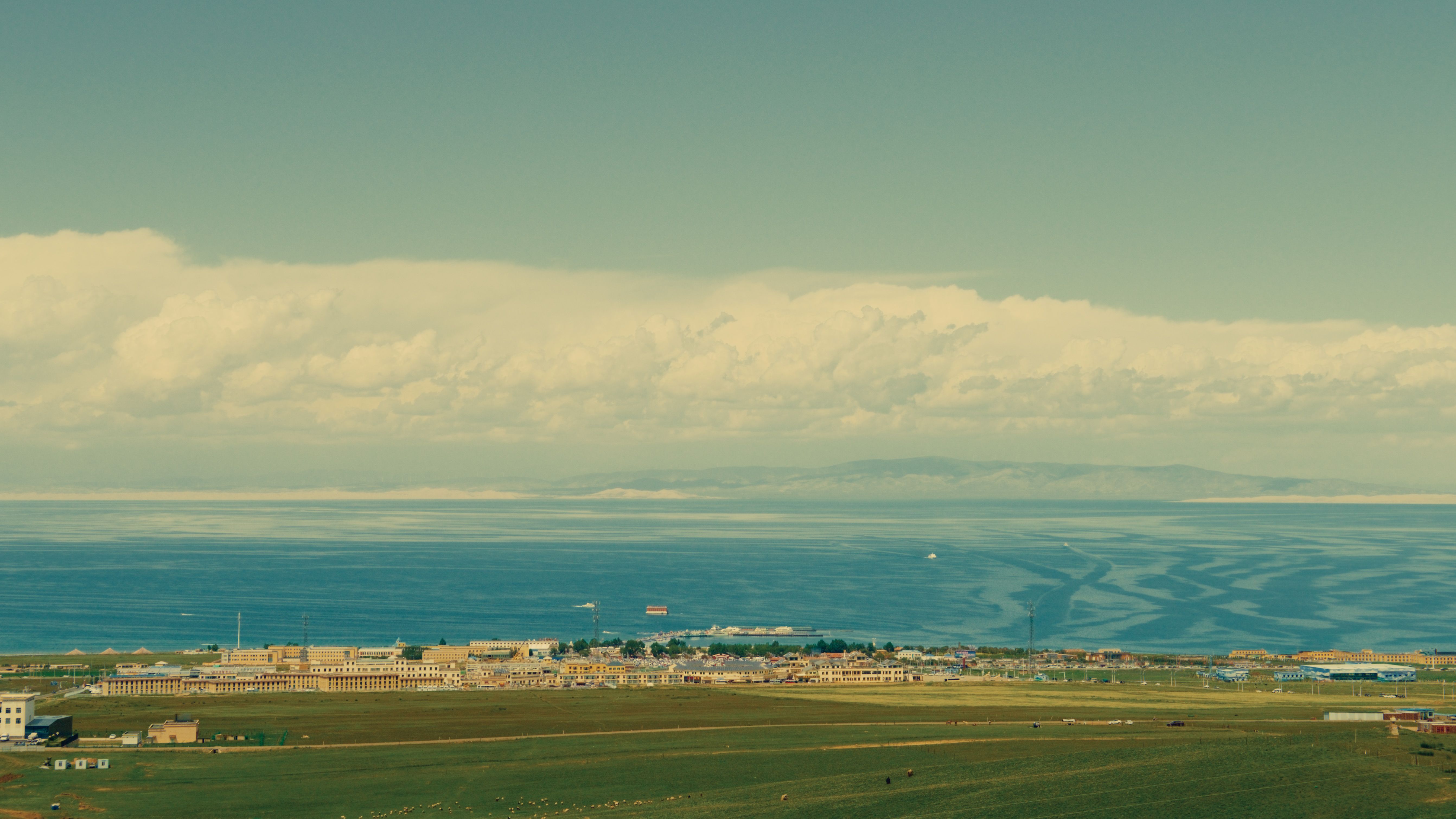 Aerial view of coastal countryside with buildings by a vast ocean under a serene sky.