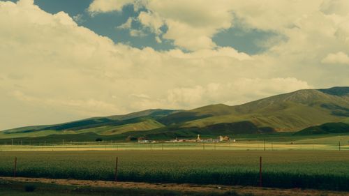 Free Expansive rural landscape with green fields, hills, and a small village under a cloudy sky. Stock Photo