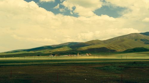 Free Lush green hills with a quaint village in the distance under a cloudy sky. Stock Photo