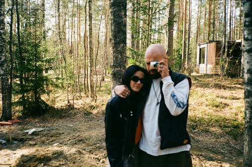 Bald Man Hugging Woman in Forest and Taking Pictures