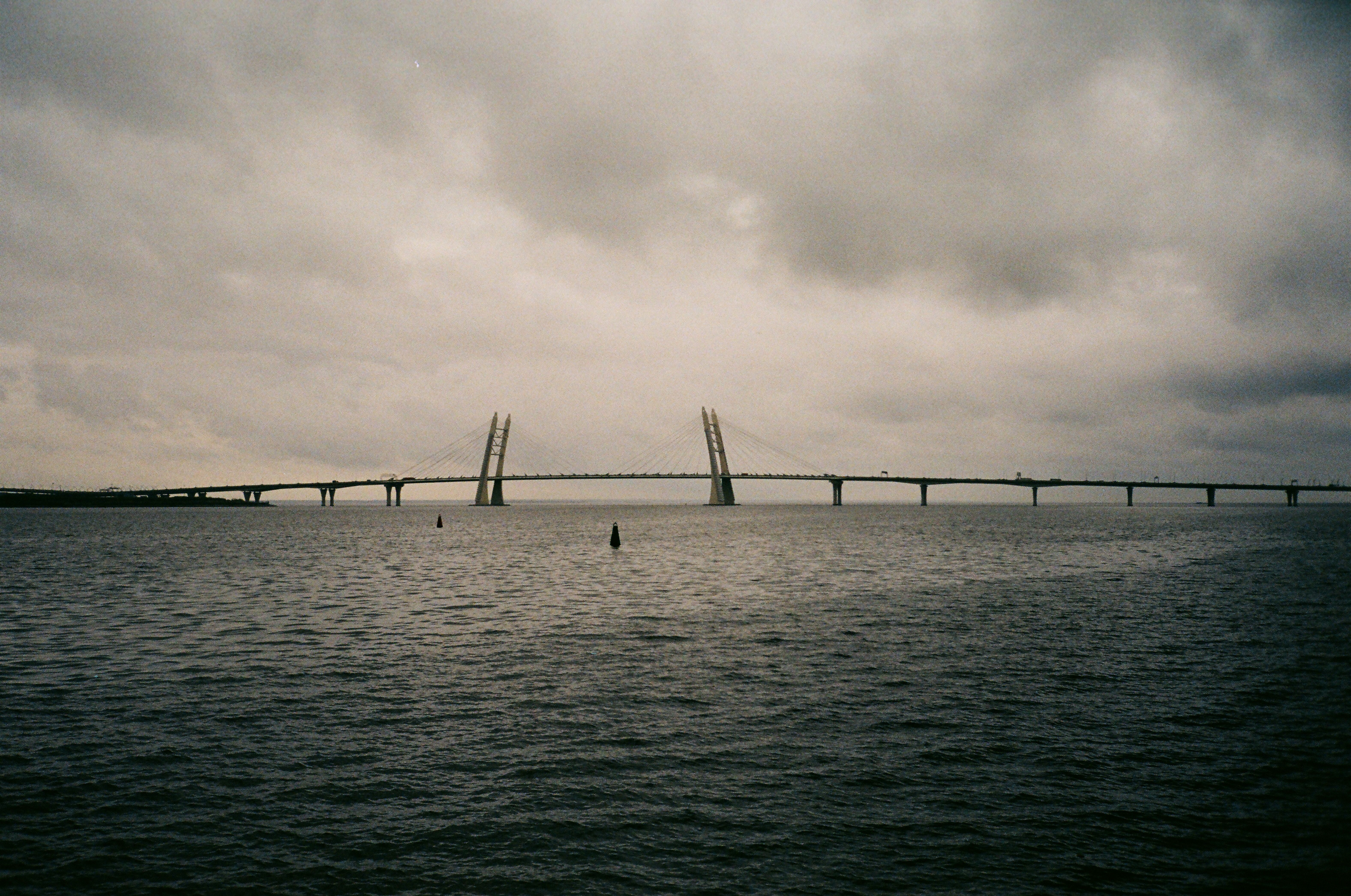Long bridge spanning over the sea under overcast skies, creating a dramatic and moody scenic view.