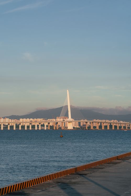 Free A stunning view of the Shenzhen Bay Bridge at sunset with a calm sea and clear sky. Stock Photo