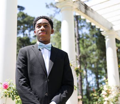 A young man in a suit and bow tie standing in front of a gazebo