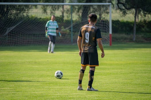 Soccer player in action preparing for a penalty kick on a sunny day in a green field.