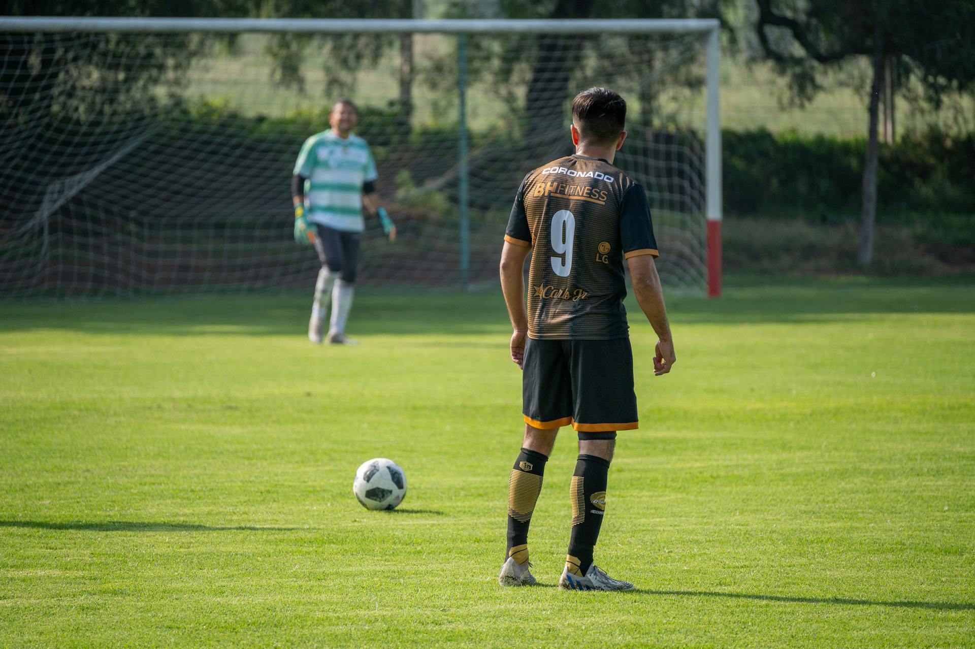 Soccer player in action preparing for a penalty kick on a sunny day in a green field.