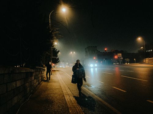Free A dimly lit urban street at night with people walking on the sidewalk. Stock Photo