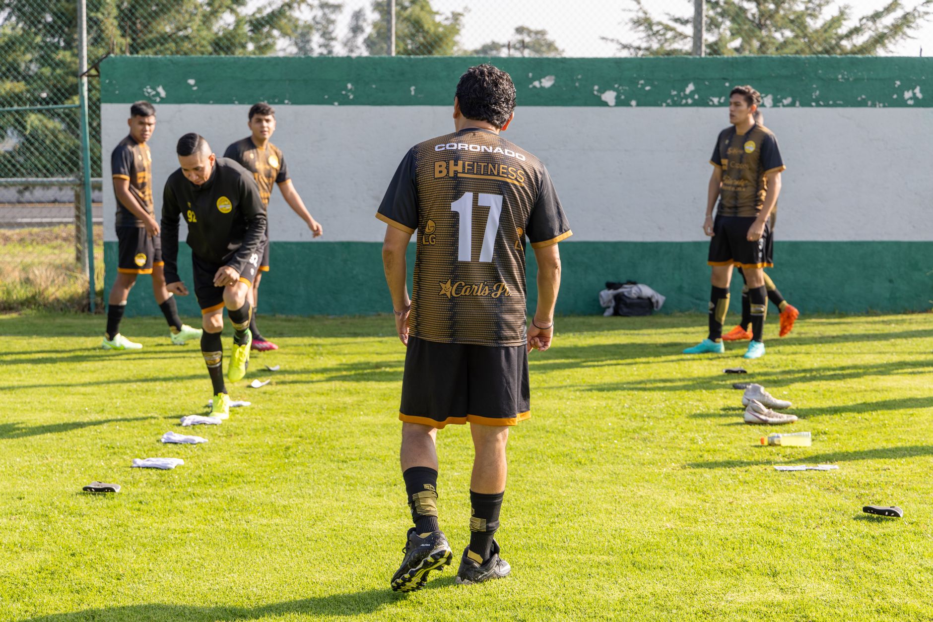 Men in matching jerseys warming up on a sunny football pitch before a match.