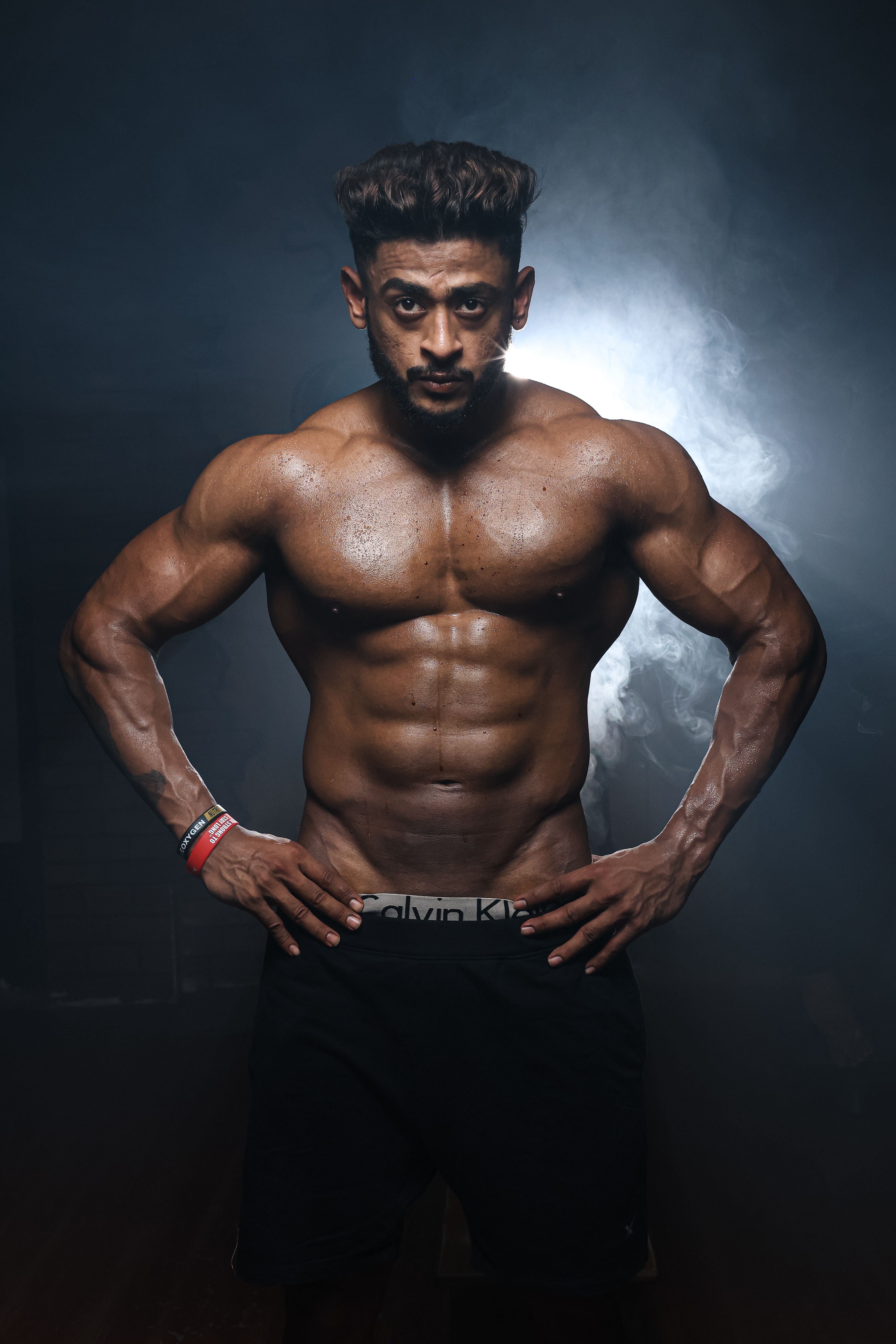 Portrait of a muscular male model posing confidently in a studio setting with a dramatic black background.