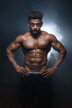 Portrait of a muscular male model posing confidently in a studio setting with a dramatic black background.