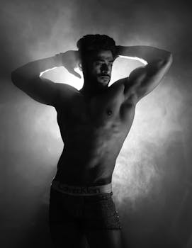 Black and white studio shot of a shirtless male model posing for a fitness photo.