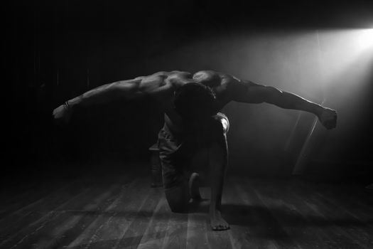 Dramatic kneeling pose of a muscular shirtless man in a black and white setting.
