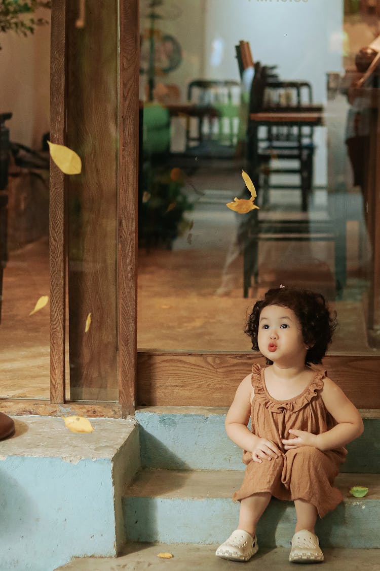 A Little Girl Sitting On The Steps And Making A Cute Face