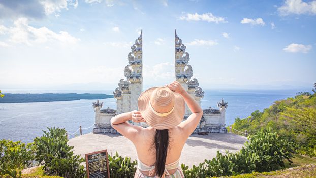 Woman in a sun hat enjoying the serene view from a Candi Bentar gateway in Bali, Indonesia.