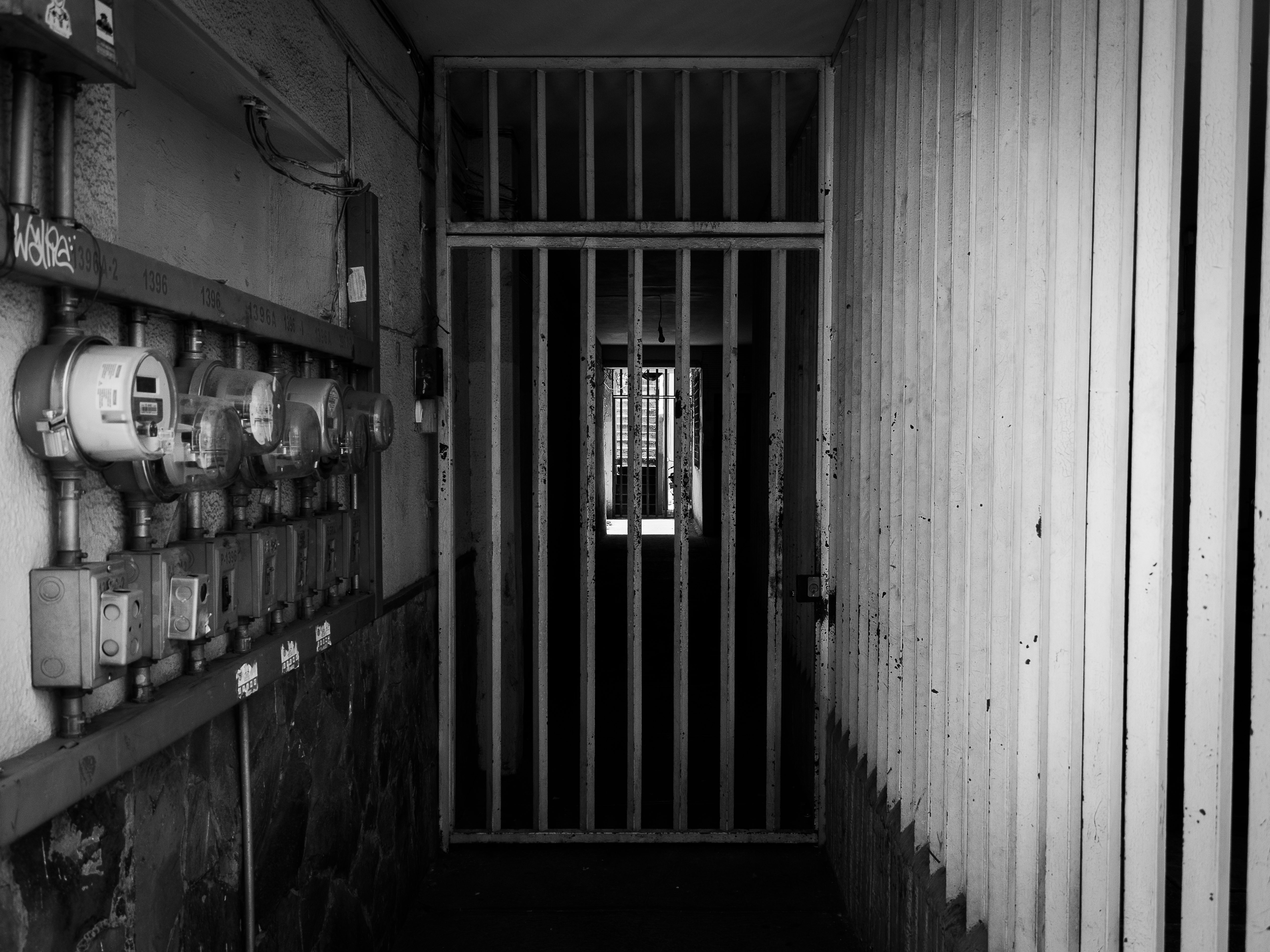 Dark corridor with iron bars and utility meters, evoking security and confinement.