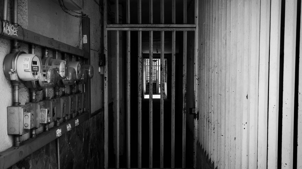 Dark corridor with iron bars and utility meters, evoking security and confinement.