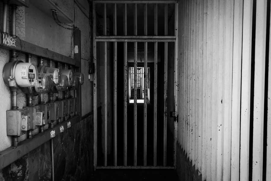 Dark corridor with iron bars and utility meters, evoking security and confinement.