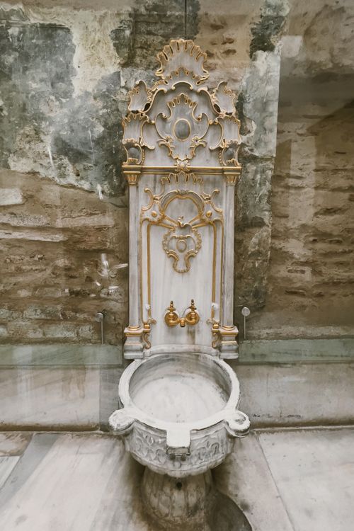 Free Elegant marble fountain with gold accents against a rustic wall. Perfect for decor and architectural themes. Stock Photo