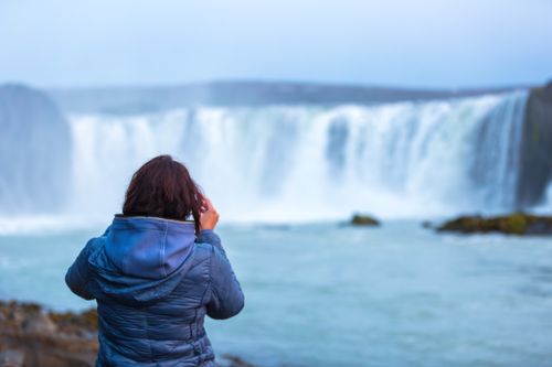 Free A woman in a blue jacket admires a breathtaking waterfall in a natural landscape. Stock Photo