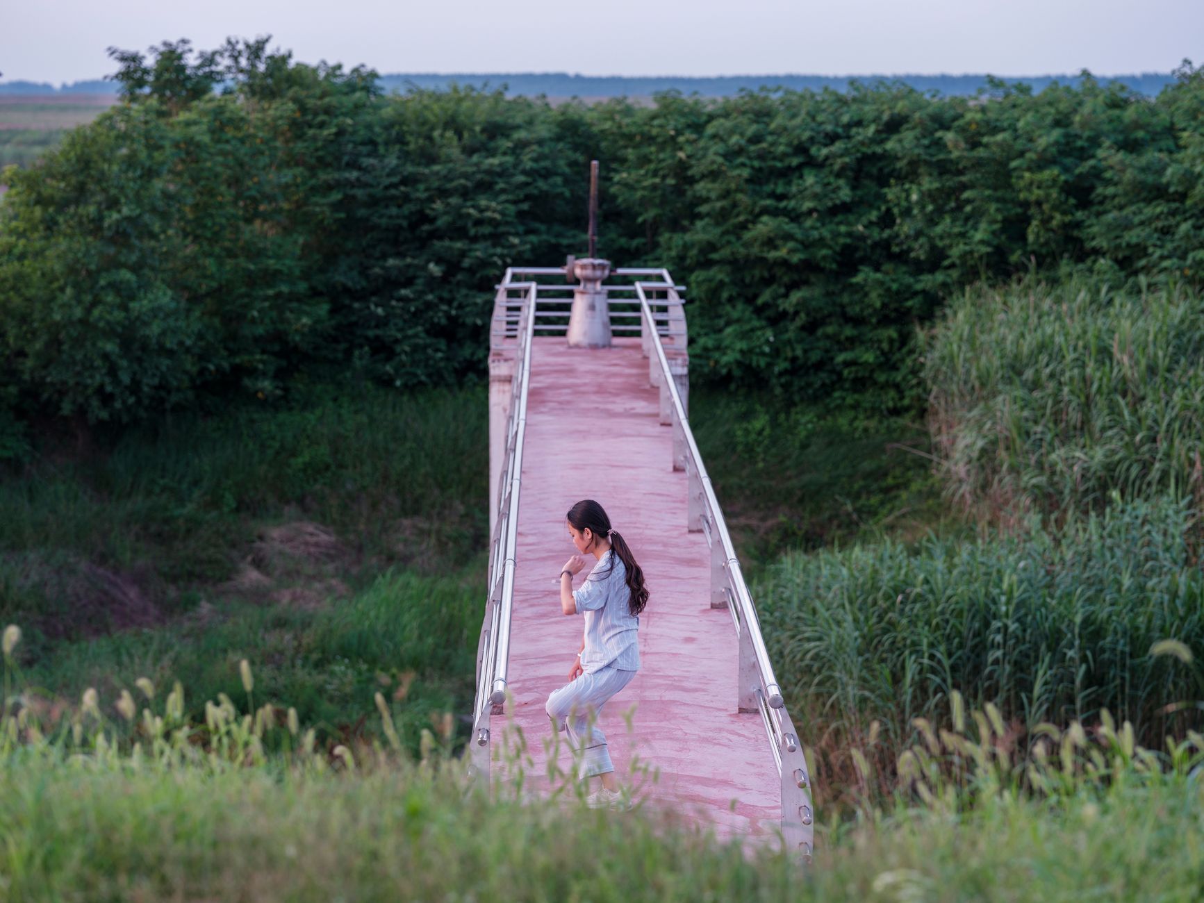 A woman meditating on a footbridge surrounded by lush greenery, offering a serene outdoor experience.