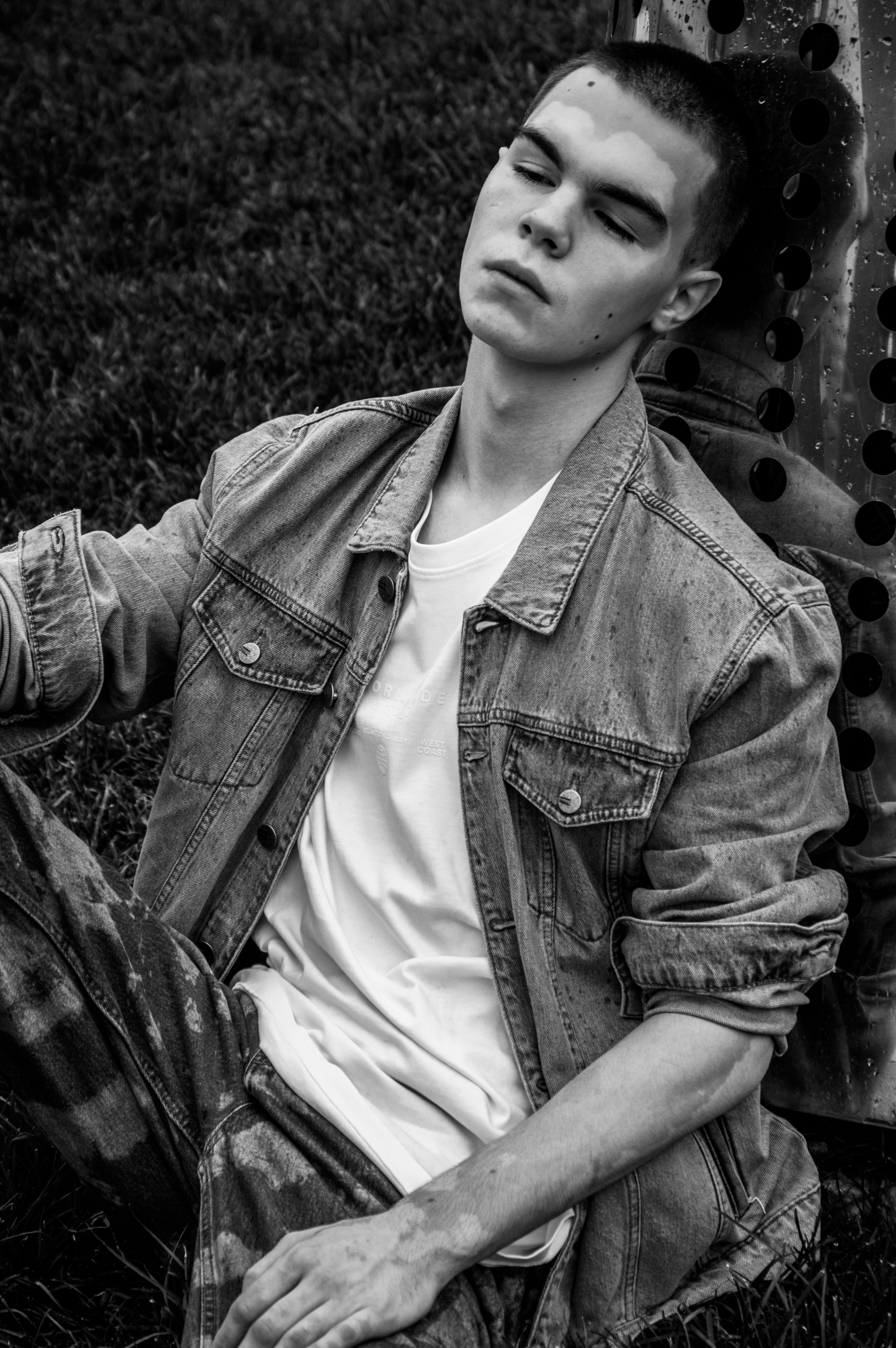 Black and white portrait of a young man relaxing outdoors with eyes closed.
