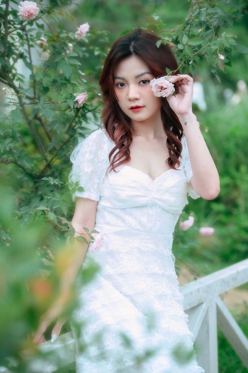 Free Young bride in white dress poses gracefully in a rose garden, exuding timeless beauty and fashion. Stock Photo